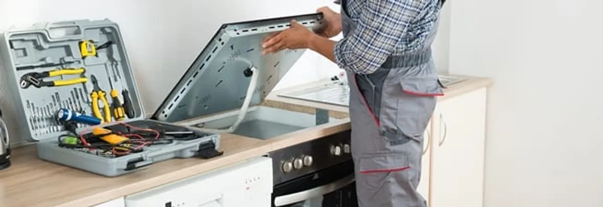 Cooktop repair technician lifting a built-in stovetop for service in Akron, OH