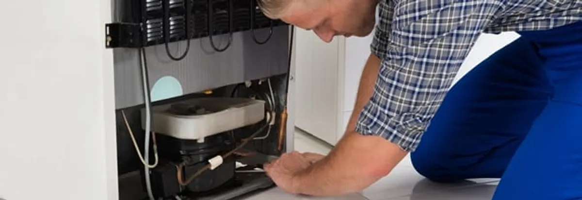 Refrigerator repair technician servicing the compressor and condenser area in Akron, OH