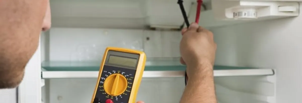 Refrigerator repair technician testing electrical components with a multimeter in Akron, OH